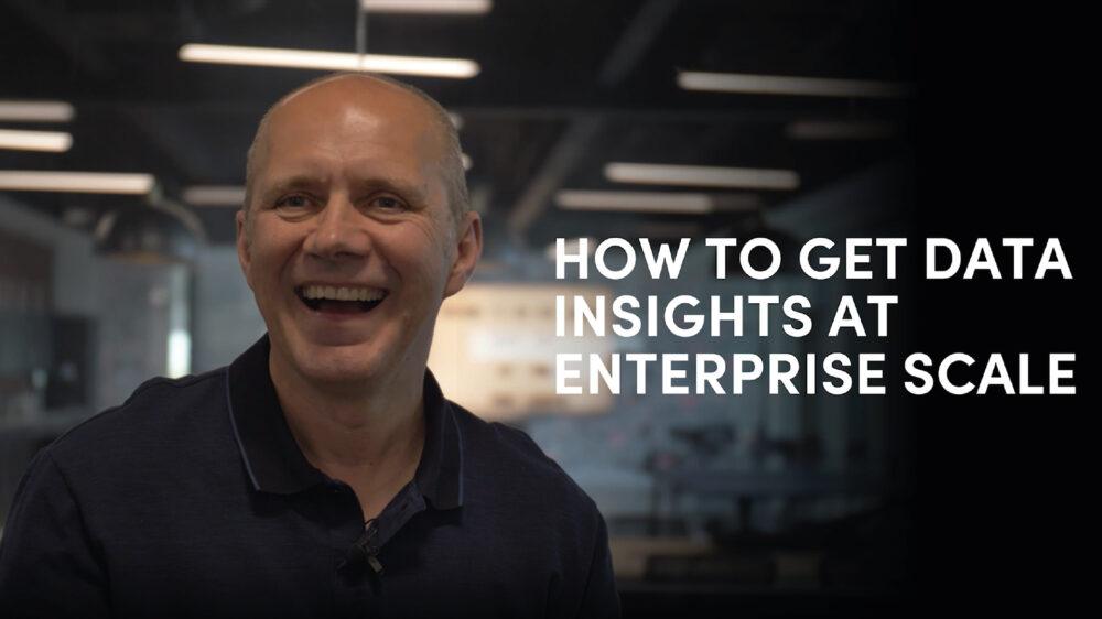 Smiling person in a dark shirt sits in an office setting. Text reads, "How to Get Data Insights at Enterprise Scale."