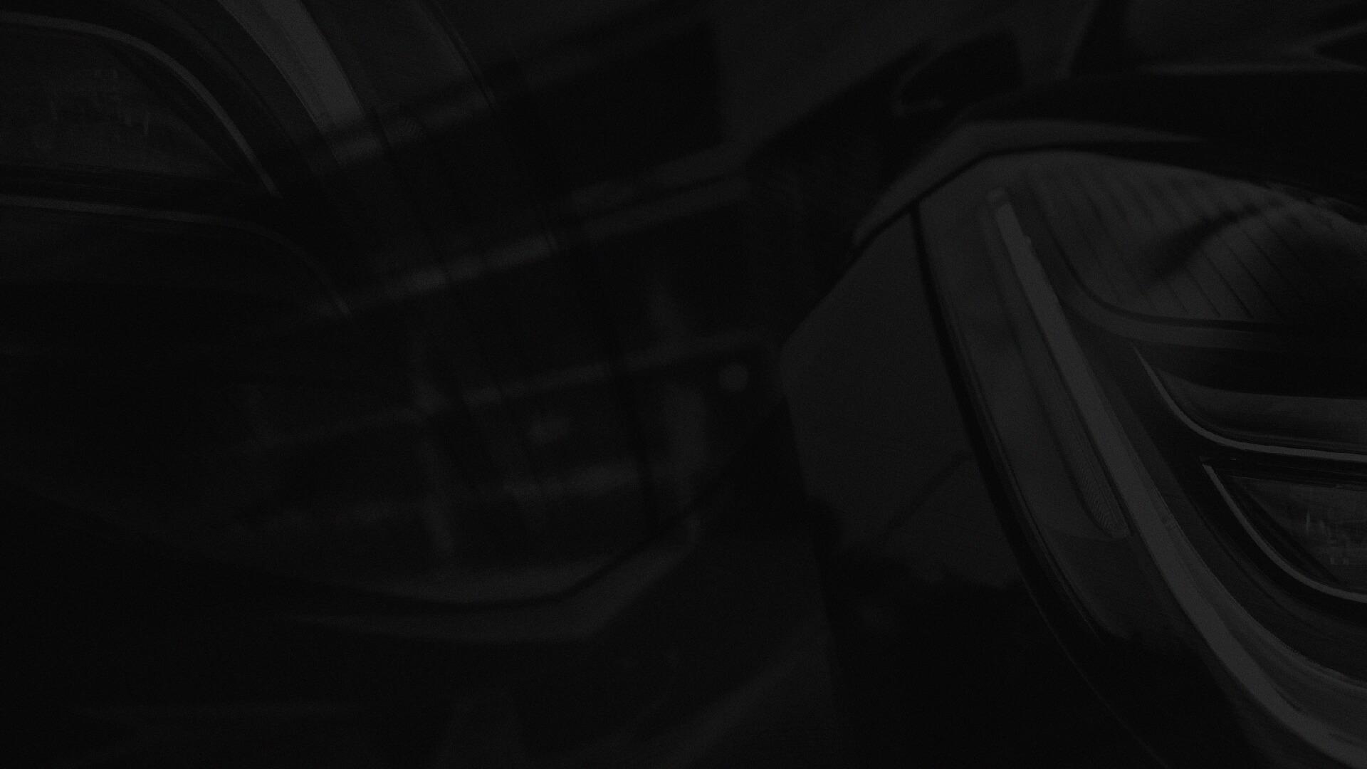 Close-up of a car's sleek, shiny headlights and side mirror, reflecting light and surrounding environment.