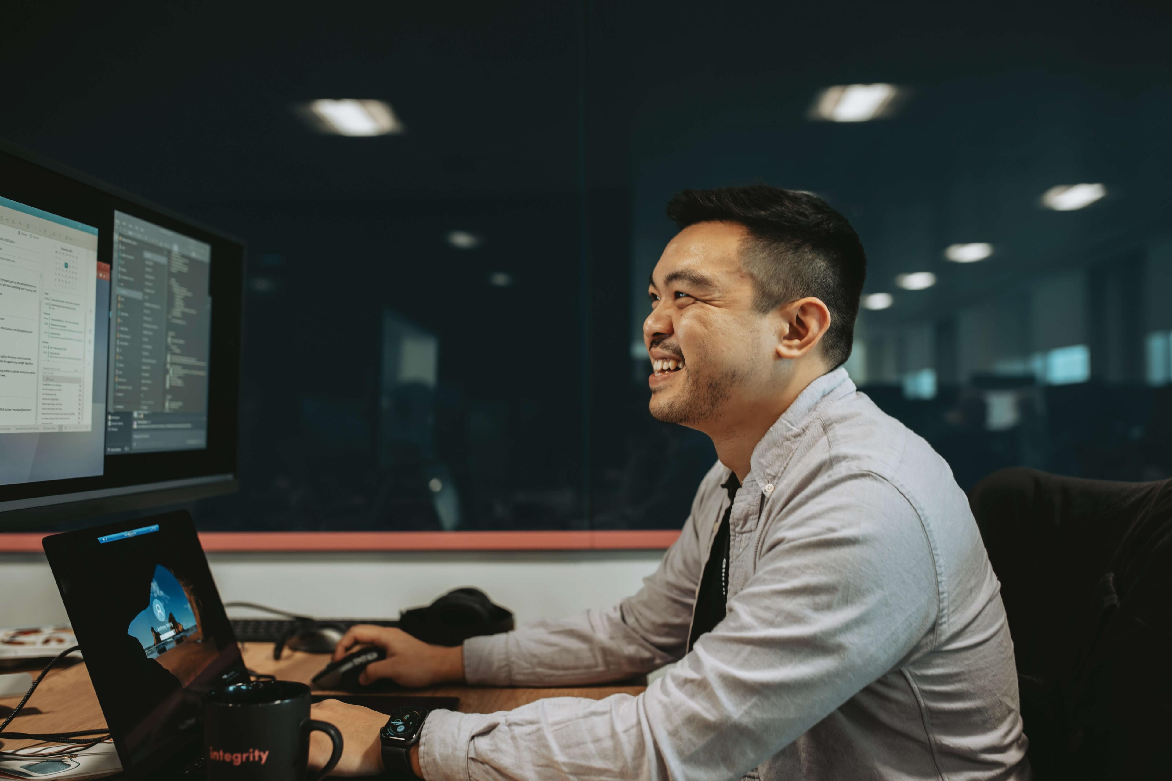 Man smiling while working on a computer in an office, with multiple screens displaying code and documents.