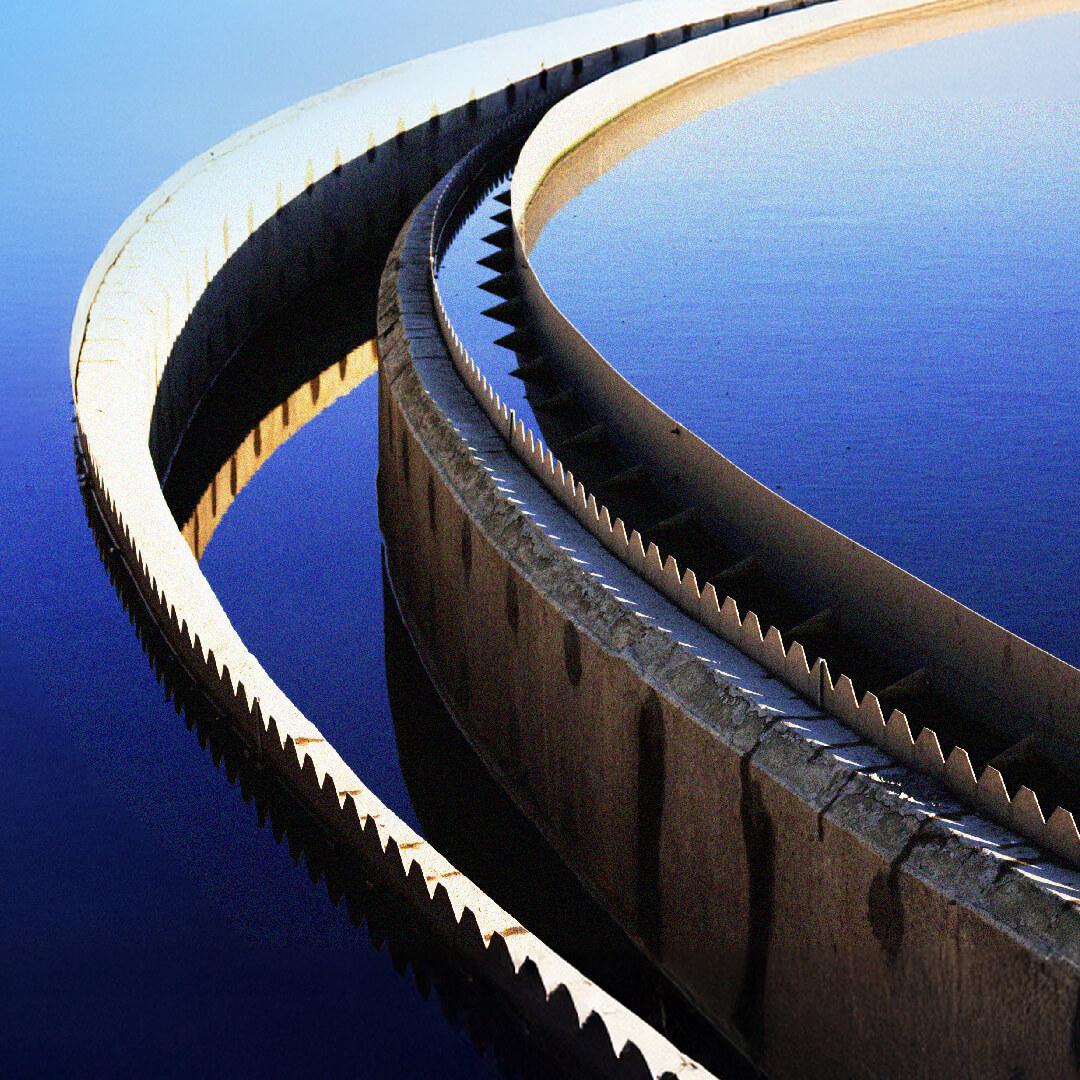 Curved, saw-toothed barriers reflecting in calm blue water, creating an abstract, symmetrical pattern.