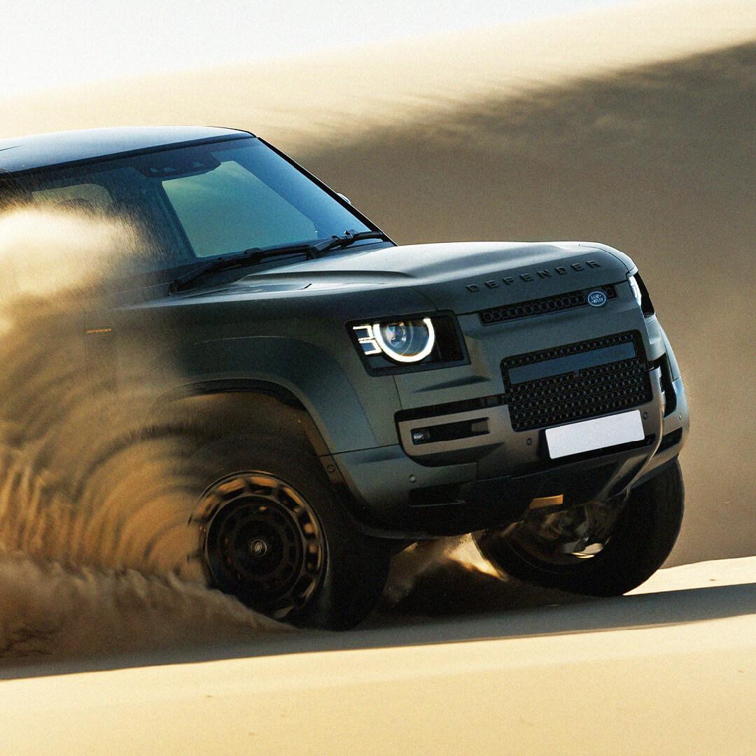 A rugged SUV powers through sandy dunes, kicking up a cloud of dust, showcasing its off-road capabilities and robust design.