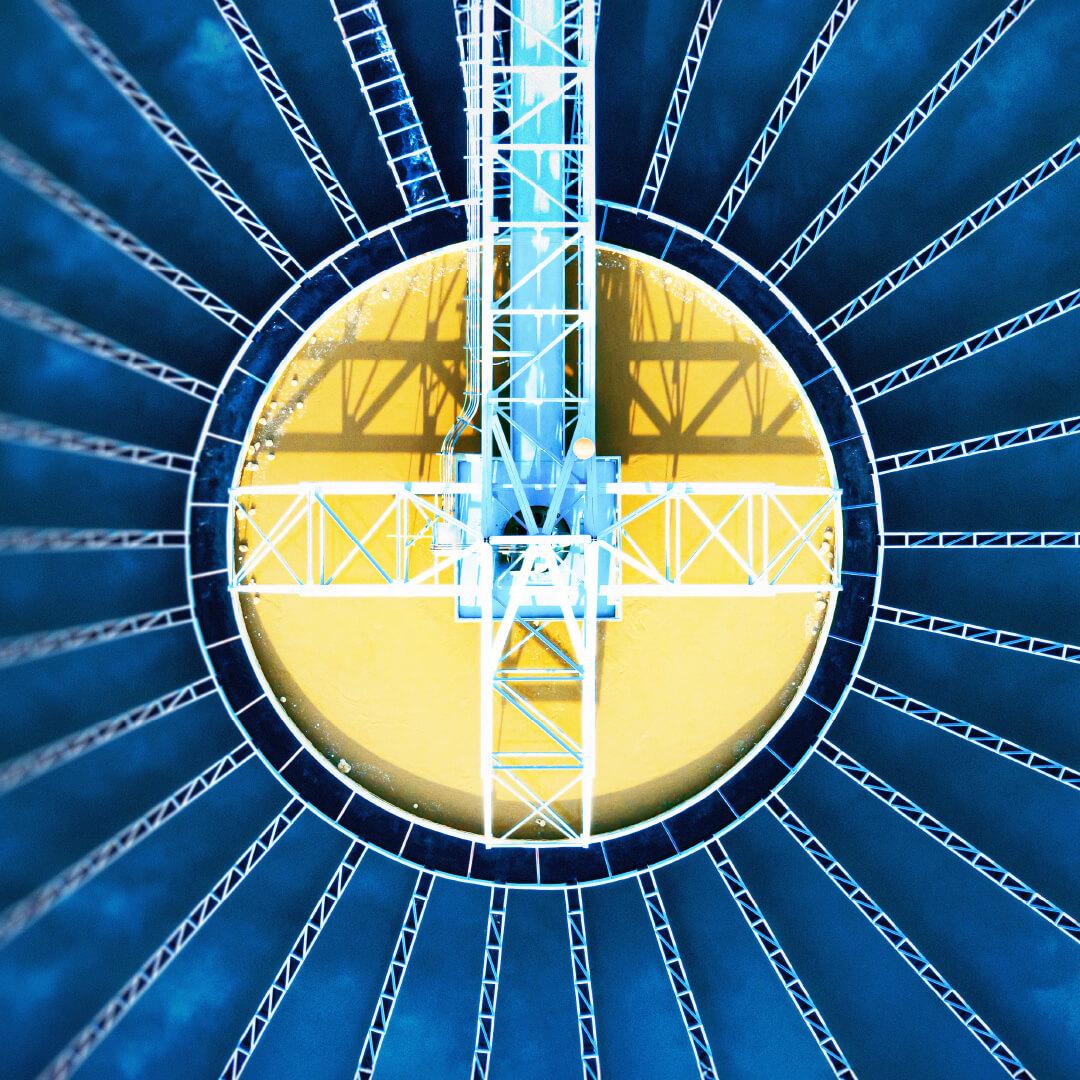 Aerial view of a circular industrial structure with radiating beams over a yellow surface, resembling a sunburst pattern.