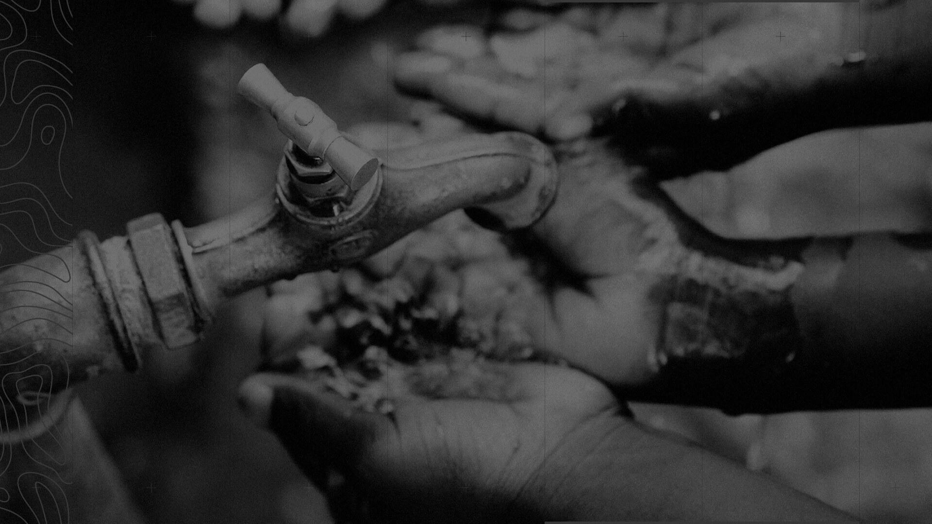 Black and white image of hands collecting water from a faucet, emphasising the importance of water access.