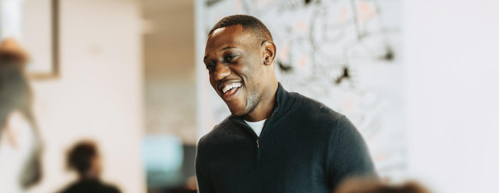 A person in a dark sweater smiling joyfully, with a blurred office background.