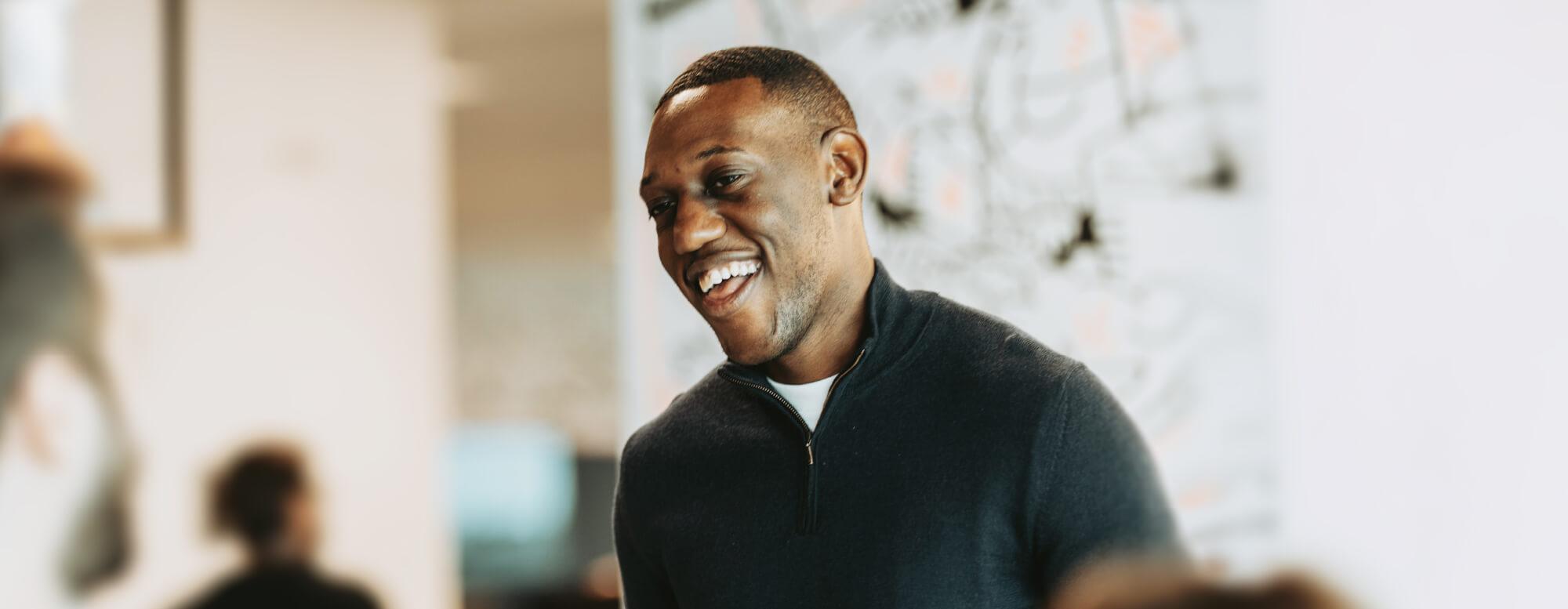 A person in a dark sweater smiling joyfully, with a blurred office background.